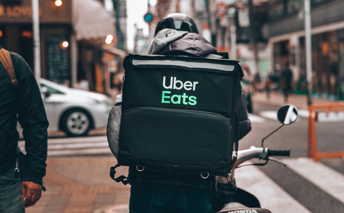 Homem de costas, em uma motocicleta, carregando uma mochila de delivery com o logotipo da Uber Eats
