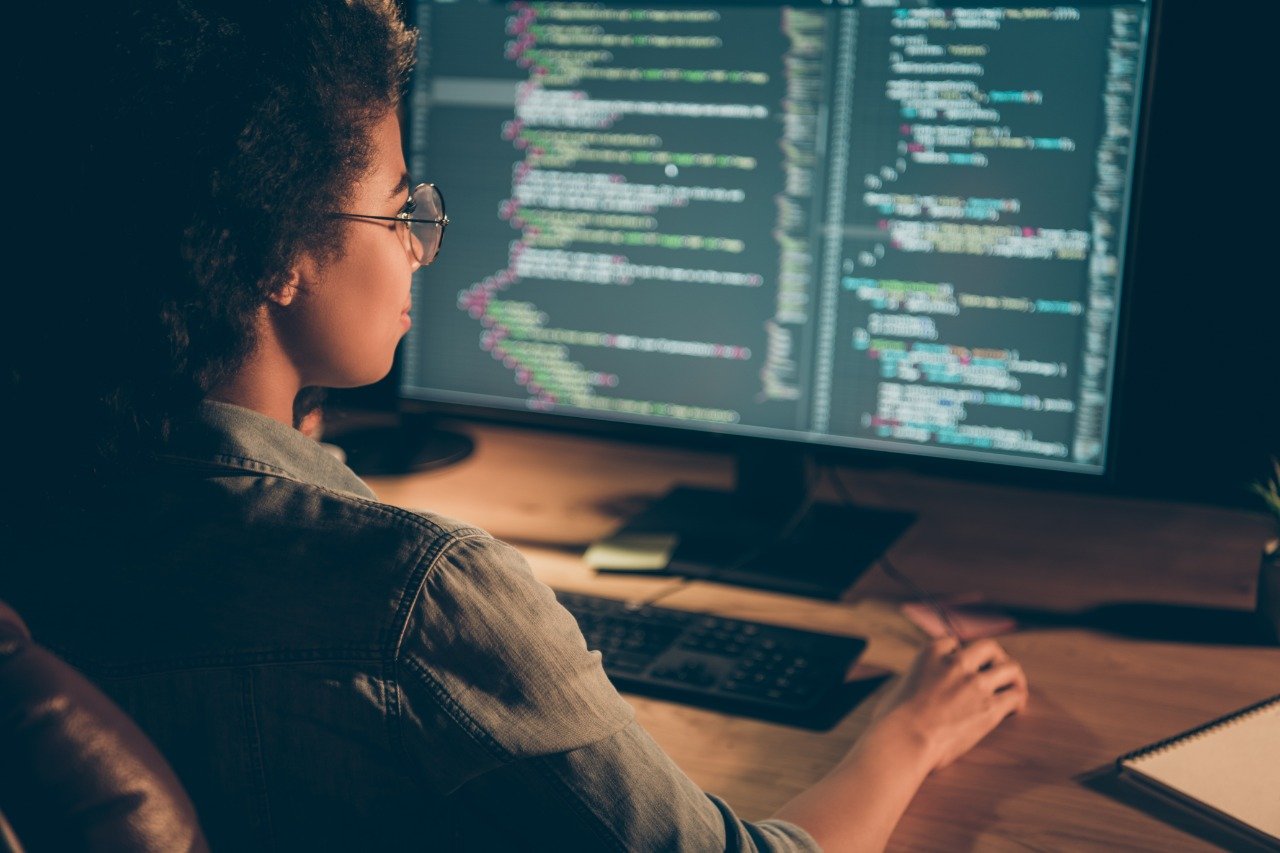 Meninas programadoras: mulher sentada em frente à tela de um computador, digitando códigos de programação