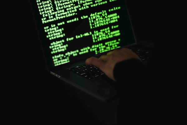 Imagem mostra uma mão digitando em um notebook, na tela aparece um código de programação em verde