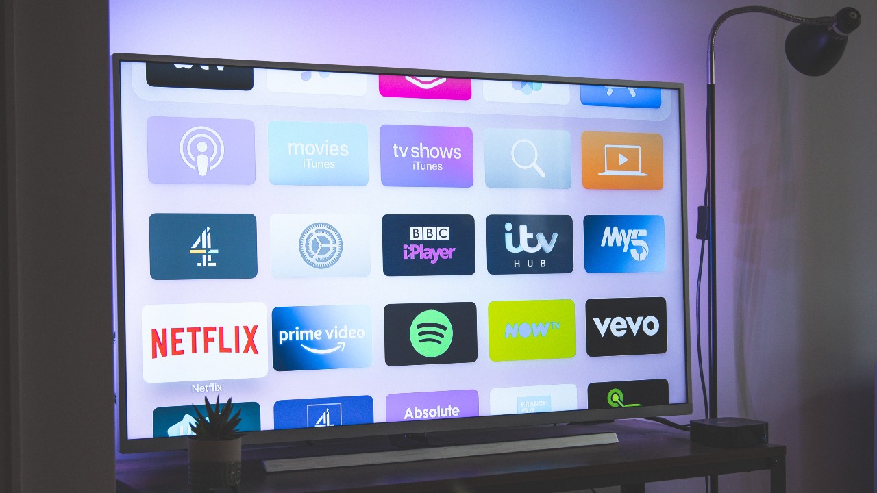 Uma televisão em cima de um móvel exibe em sua tela diversos aplicativos de streaming, incluindo Netflix, Amazon Prime Video, Spotify, entre outros