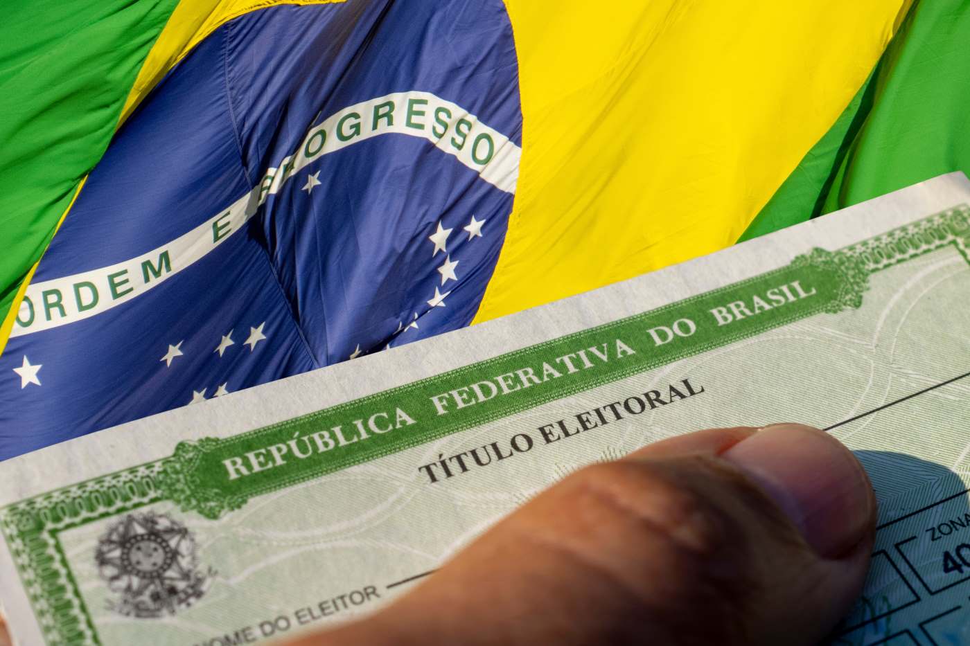 Título de eleitor exibido à frente de uma bandeira do Brasil. TSE pede cuidado com fake news políticas veiculadas em época de eleição