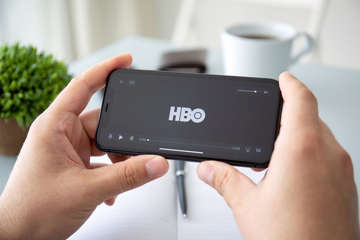 Mão masculina segura um iPhone, na tela do smartphone aparece o logotipo da HBO