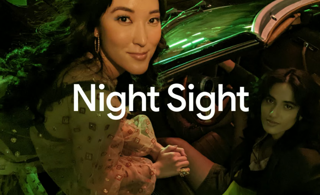 Ma imagem aparecem duas mulheres, uma sentada dentro de um carro e a outra apoiada no espelho retrovisor ao lado da janela; à frente está o texto "Night Sight", recurso do Pixel 6A que permite tirar boas fotos noturnas