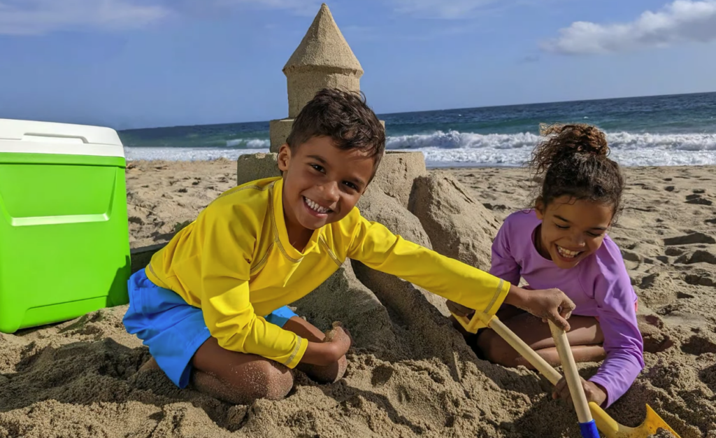 Foto de duas crianças, um menino e uma menina, brincando de castelo de areia na praia: a imagem foi usada durante o Google I/O 2022 para apresentar o recurso de edição de fotos "Magic Eraser" do Pixel 6A