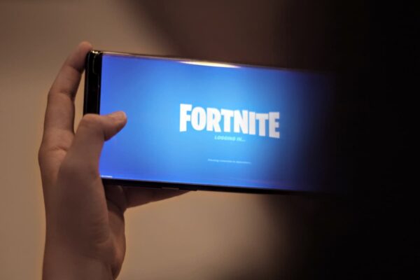 Mão segurando um smartphone que exibe em sua tela o nome do game Fortnite