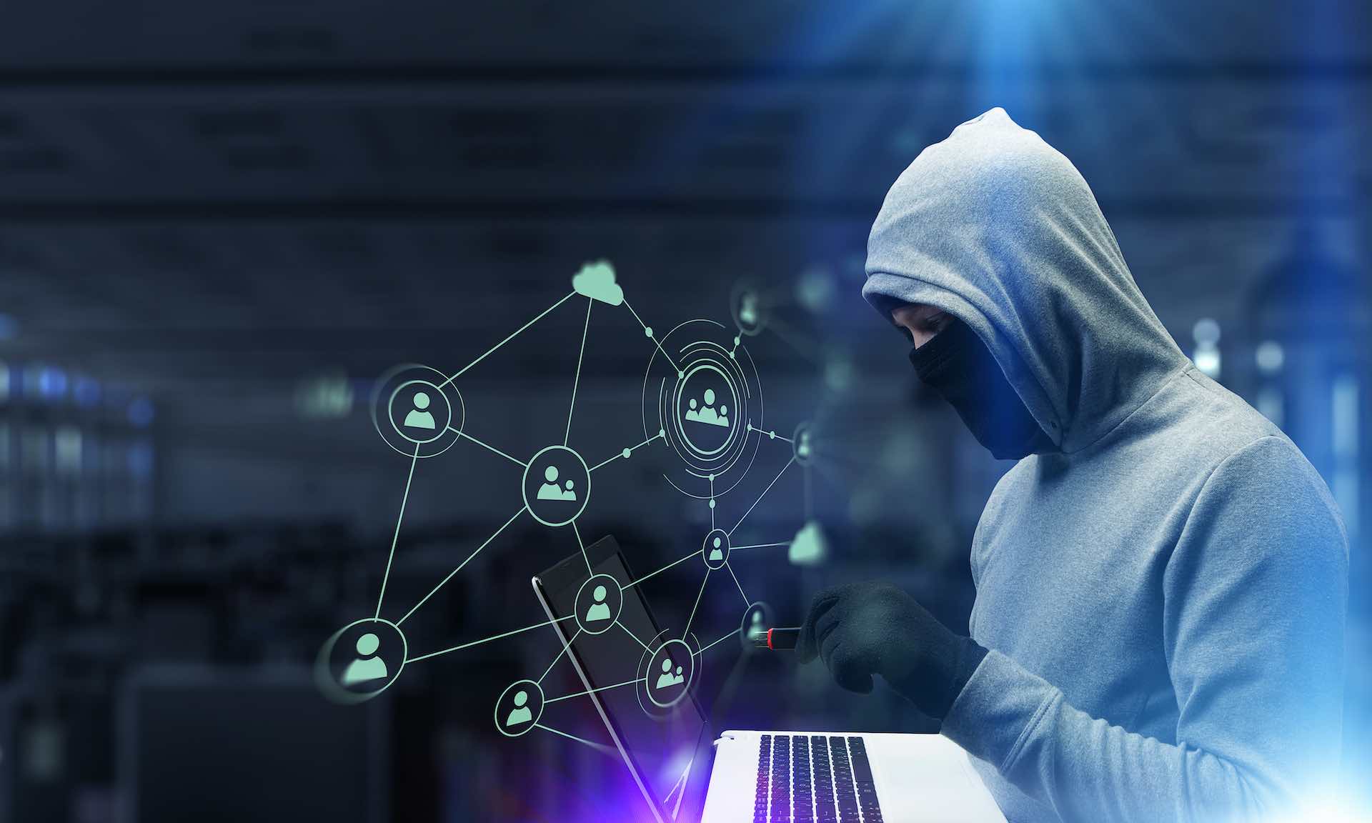 Ilustração mostra pessoa vestindo um moletom com capuz e mexendo em um notebook, representando temas como fraude, golpe, hacker, redes sociais