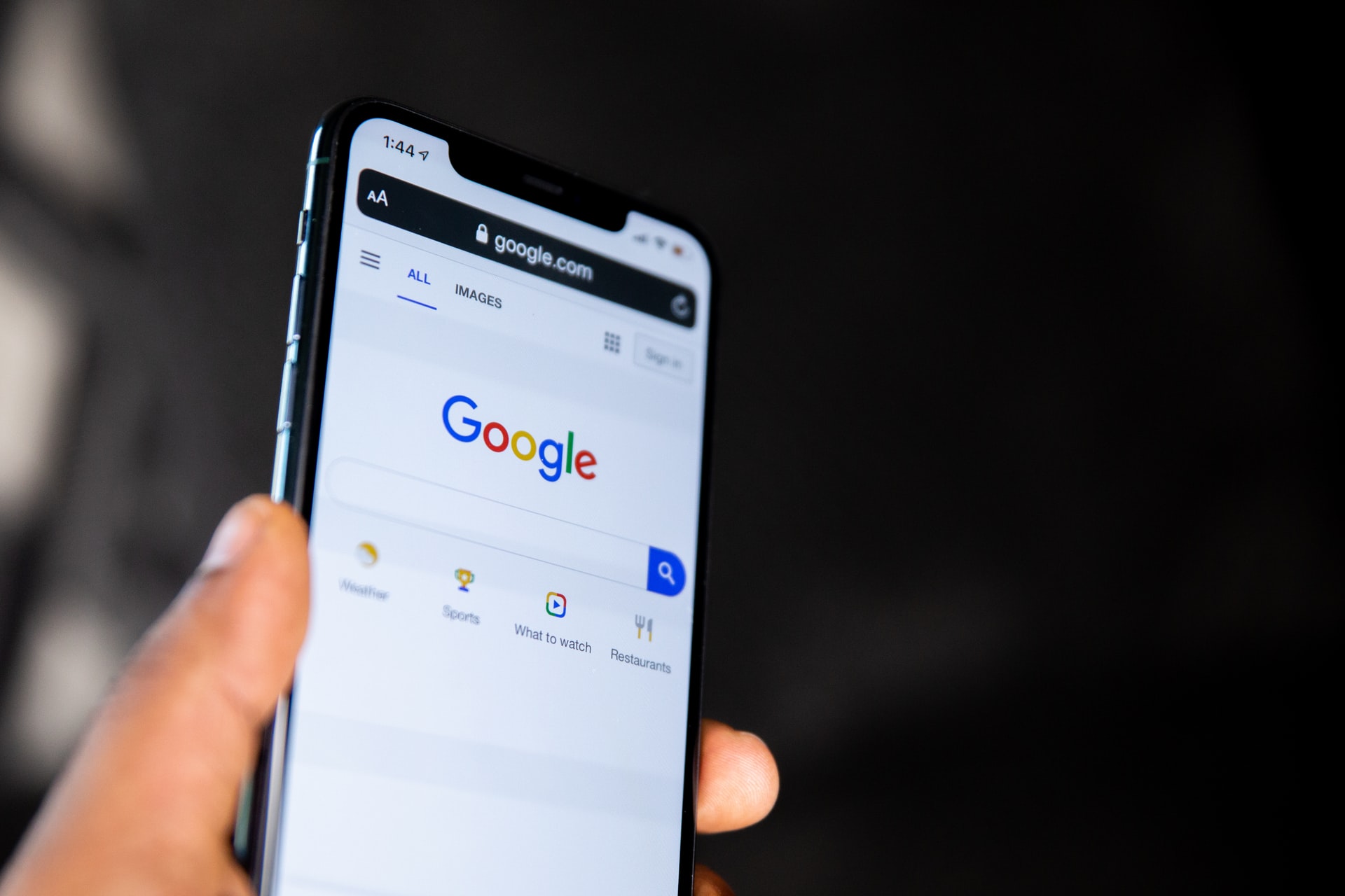 Imagem mostra um smartphone segurado em uma mão, com a tela inicial do Google aberta em seu display