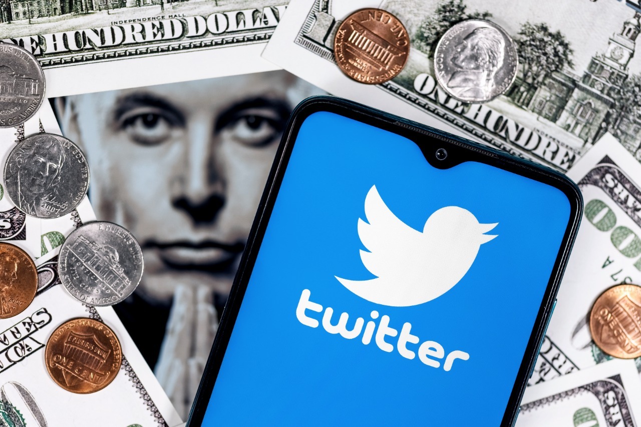 Montagem mostra o Twitter exibido em um celular, com notas de dólares ao fundo e o rosto de elon musk em preto e brando desfocado do centro