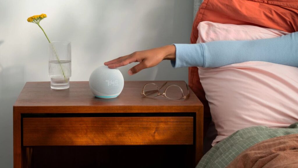 Echo Dot da Amazon em cima de uma mesa de cabeceira, sendo tocado por uma mão