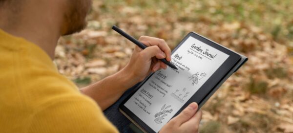 Um homem de camiseta amarela aparece de perfil e mostra que está escrevendo no e-reader Kindle Scribe, da Amazon