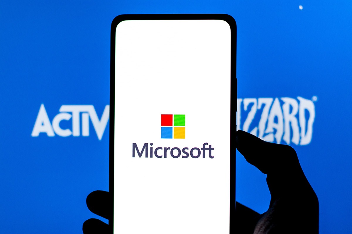 Imagem mostra um smartphone com o logotipo da Microsoft na Tela, com o logotipo da Activision Blizzard ao fundo