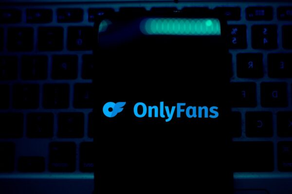 Imagem mostra a logomarca do OnlyFans, num fundo preto em uma sala de luz azul escura