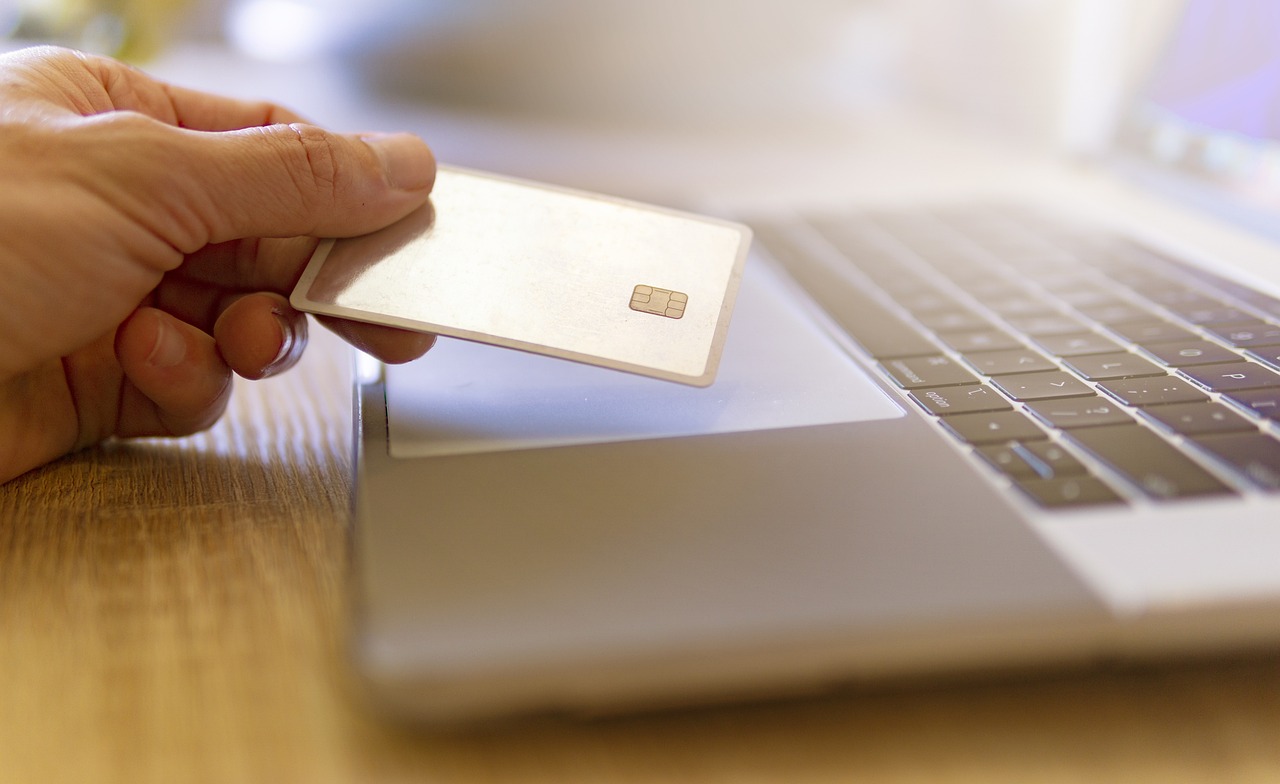 Imagem mostra um cartão de crédito apontado para um notebook, simbolizando compras online