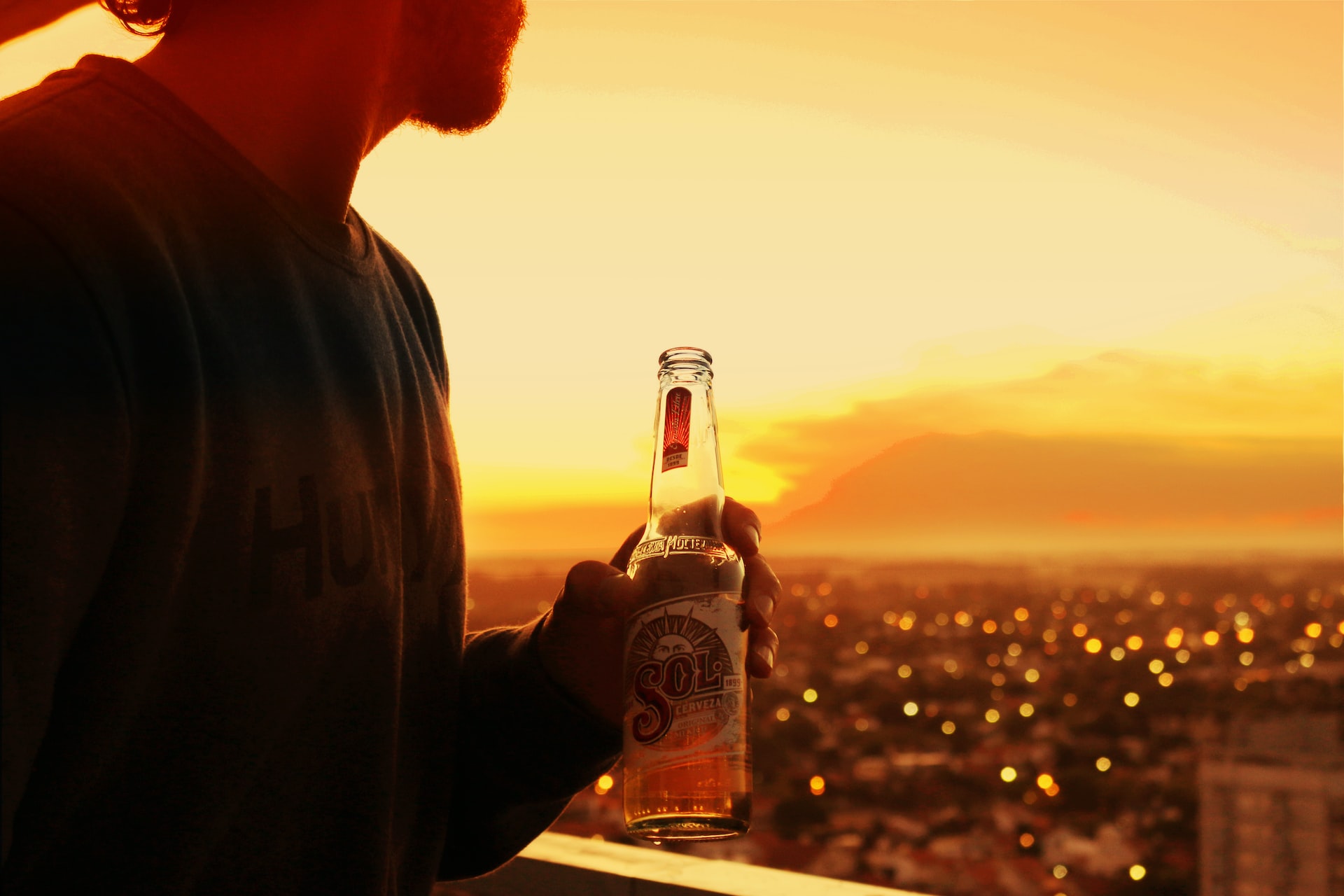 Imagem de um homem segurando uma cerveja enquanto observa o por do Sol