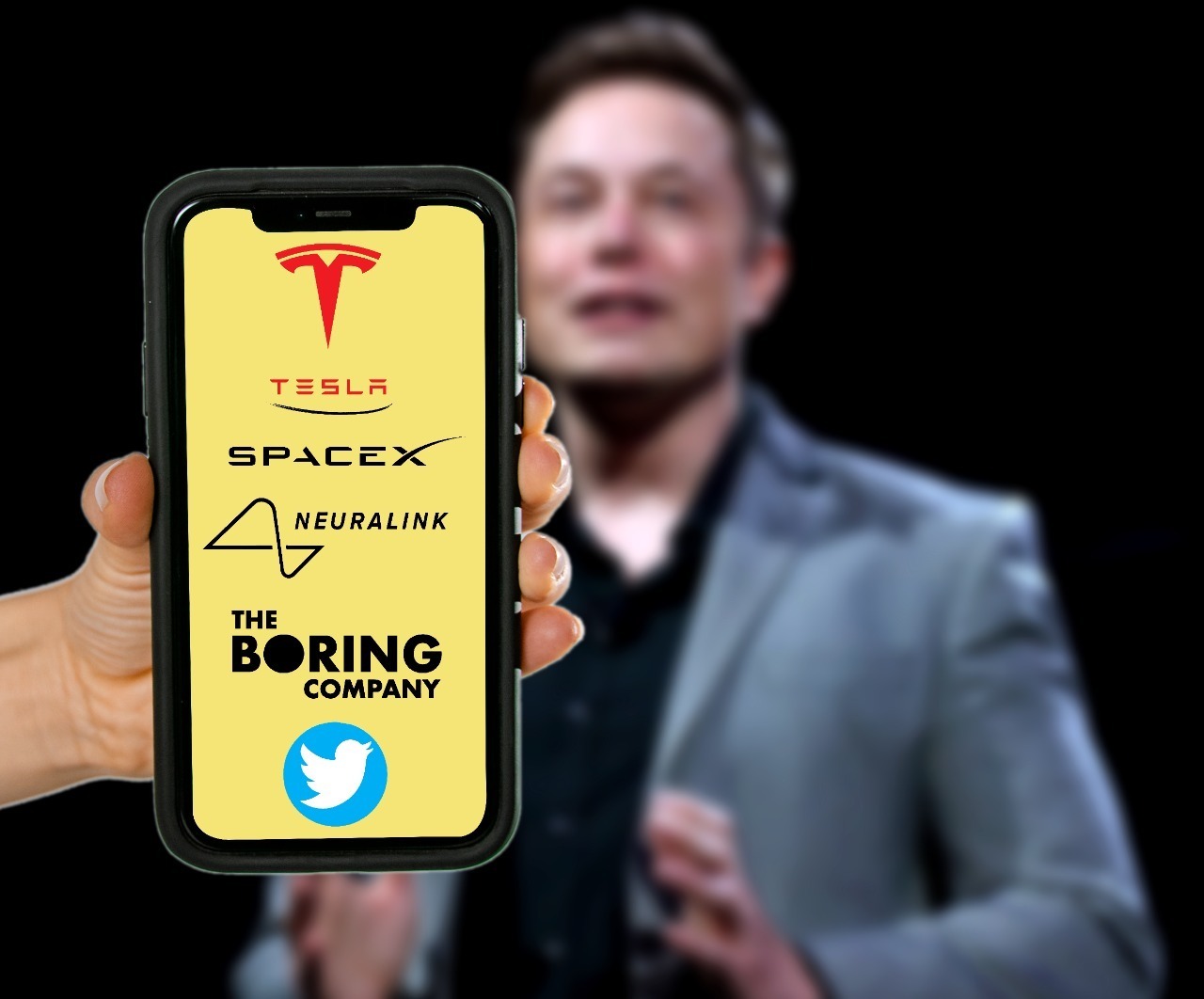 Montagem mostra um celular com todas as empresas lideradas por Elon Musk na tela, e o próprio Musk desfocado no fundo