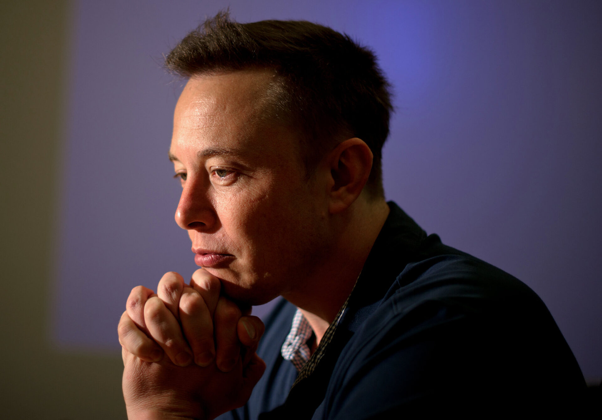 Imagem mostra o bilionário Elon Musk, atual CEO do Twitter, sentado com o queixo pousado sobre as mãos, com um rosto contemplativo