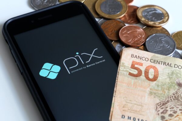 Imagem mostra um celular com logotipo do Pix e várias cédulas e moedas do Real em volta