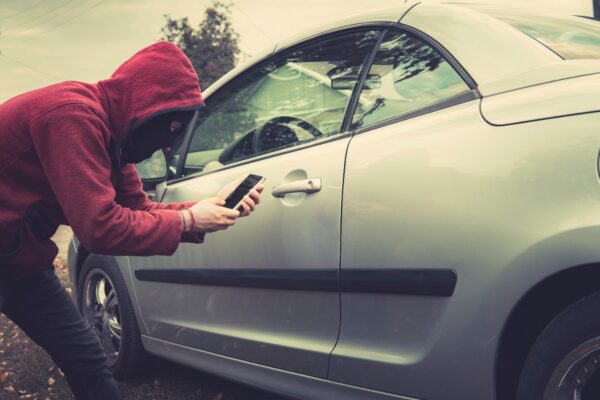 Imagem de um homem usando um celular para roubar um carro