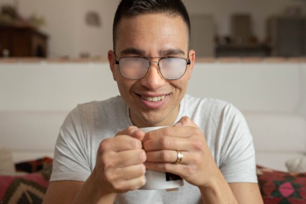 Imagem mostra homem sorridente com lentes de óculos embaçadas por causa de uma xícara de café