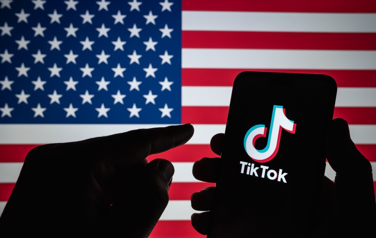 Imagem mostra o logotipo do TikTok com a bandeira dos Estados Unidos ao fundo