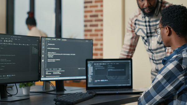 Focused software developer writing code on laptop looking at multiple screens with programming language