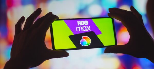 Mãos seguram um smartphone que exibe os logotipos dos serviços HBO Max e Discovery na tela