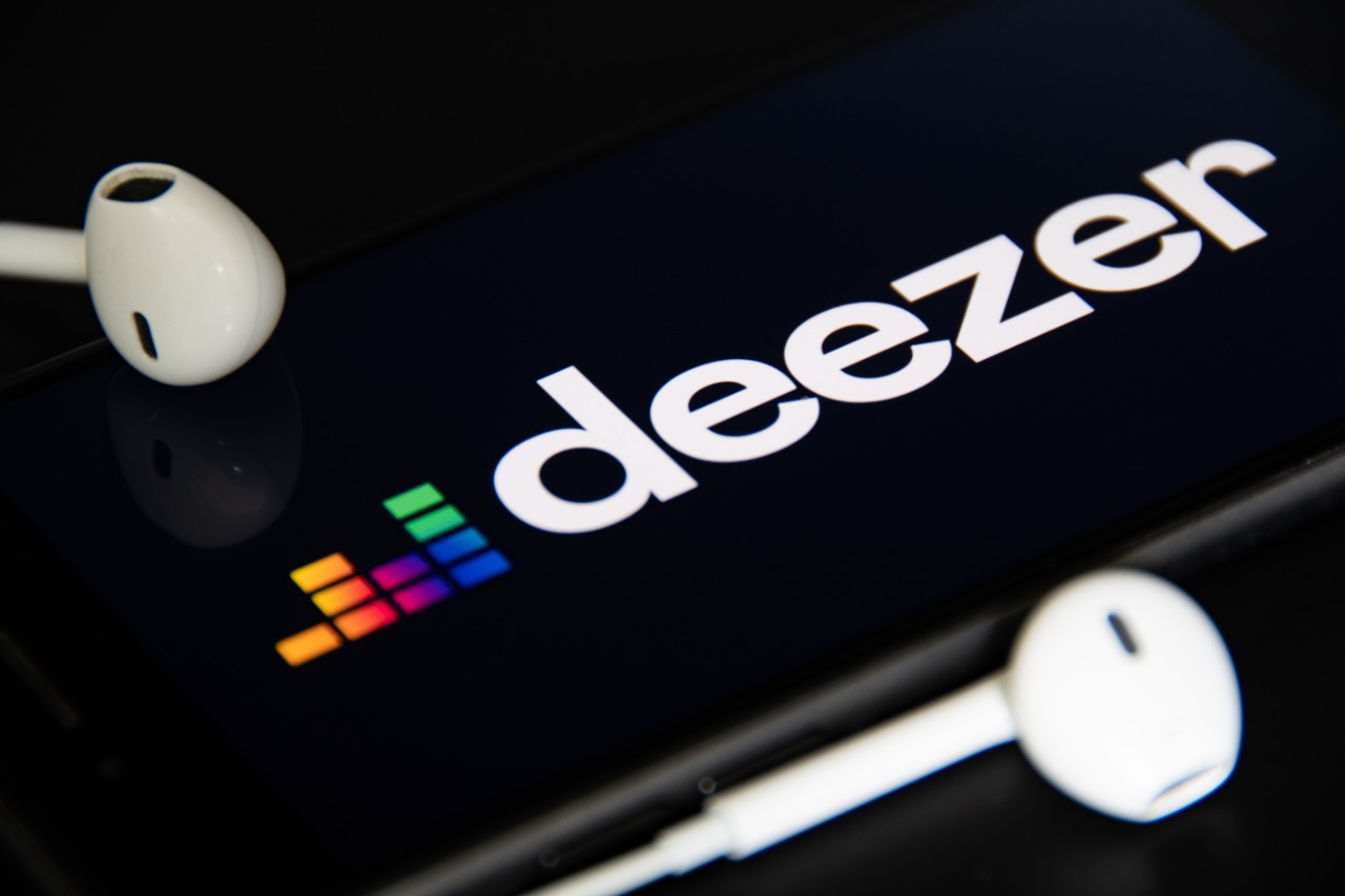 Imagem mostra o logotipo do Deezer em uma tela de smartphone, com dois fones de ouvido ao lado