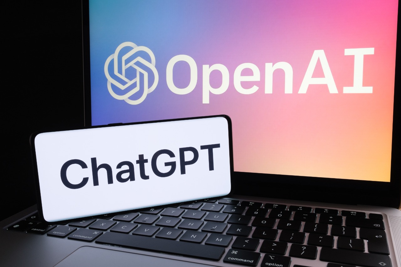 Imagem: mostra o ChatGPT nomeado em um smartphone, à frente de um notebook com o logotipo da OpenAI