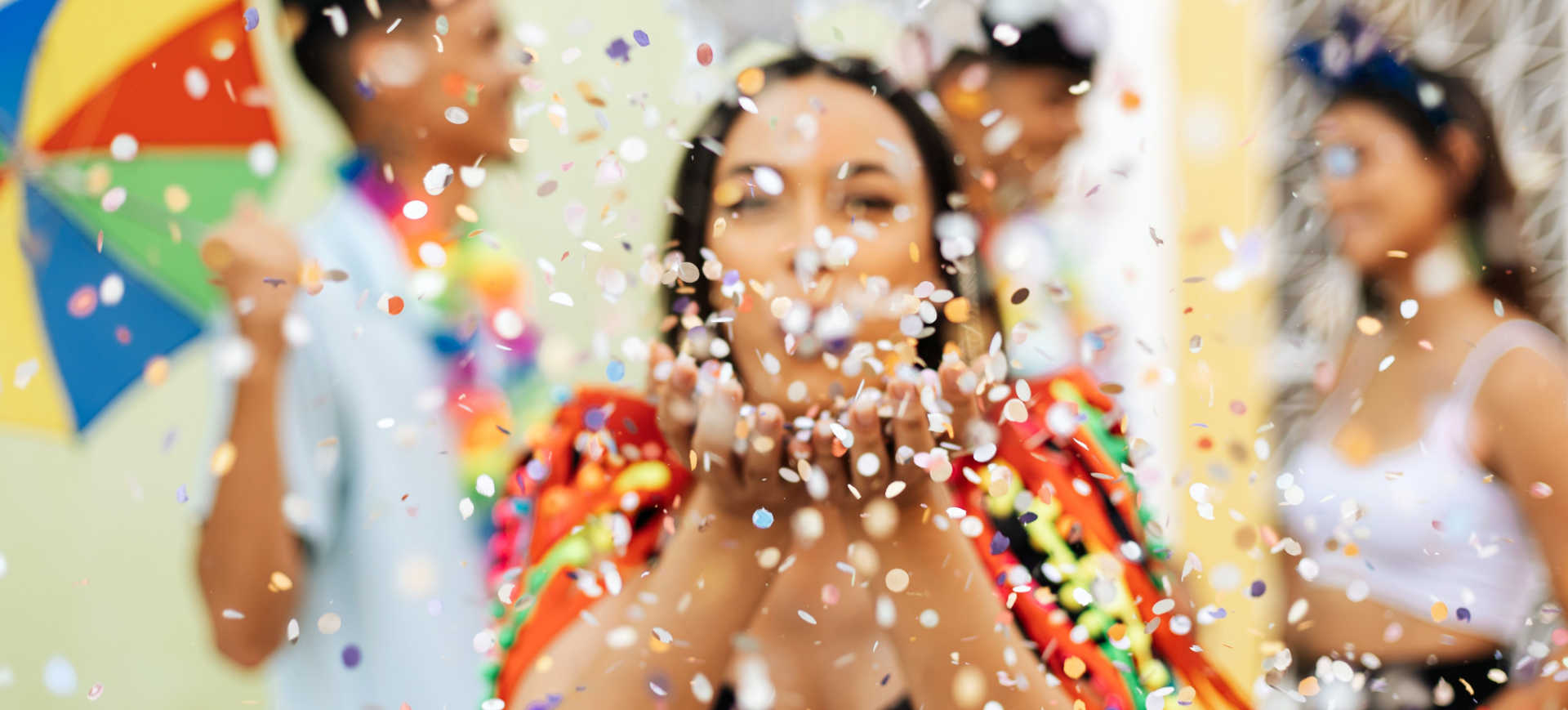 Imagem de uma mulher soprando confetes no meio da rua em um bloco de Carnaval