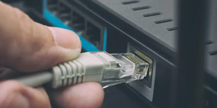 Imagem mostra um cabo Ethernet sendo inserido na traseira de um roteador de internet