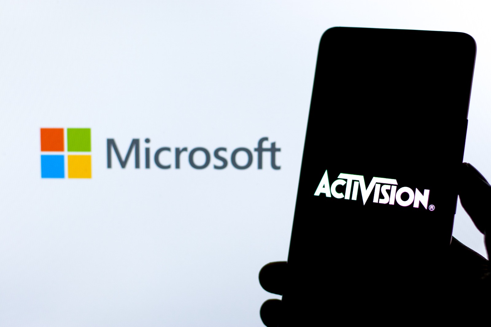 Imagem mostra o logotipo da Microsoft em um telão ao fundo, com um smartphone iluminando o logo da Activision no display