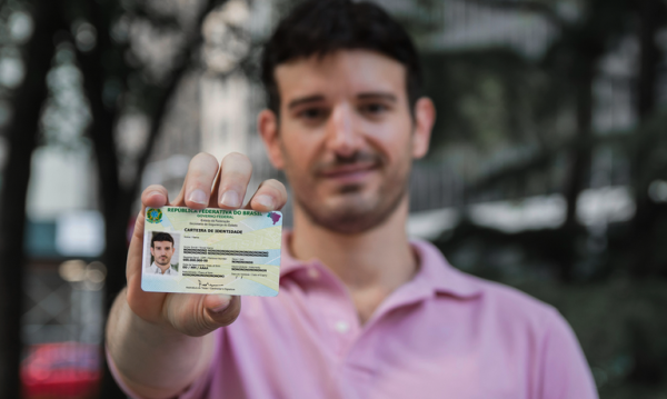 Imagem mostra um homem de camisa rosa segurando a Carteira de Identidade Nacional, novo documento de identificação pessoal emitido pelo Governo Federal