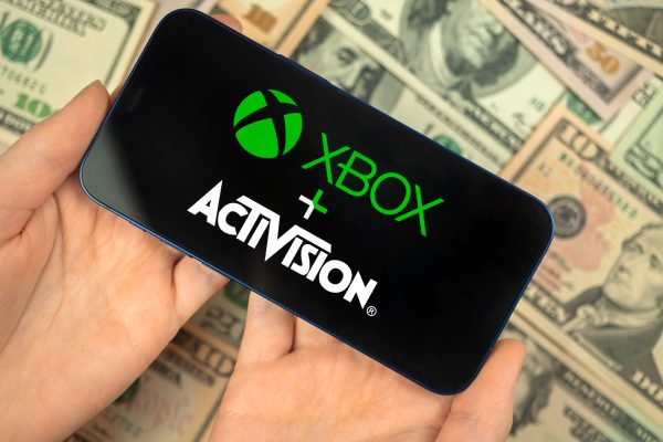 Imagem mostra smartphone com logotipos do Xbox (Microsoft) e Activision, e ao fundo, várias notas de dólares americanos