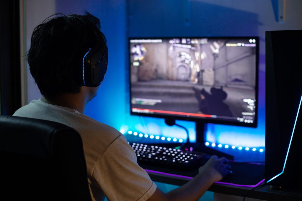 Imagem de um jovem à frente de um computador que está rodando um jogo de tiro, simbolizando jogos violentos