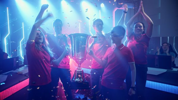 Imagem mostra um time de eSports celebrando uma vitória ao redor de um troféu