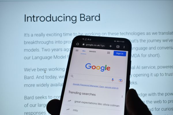 Imagem mostra um smartphone aberto na tela de buscas do Google, com o documento de apresentação do Bard ao fundo