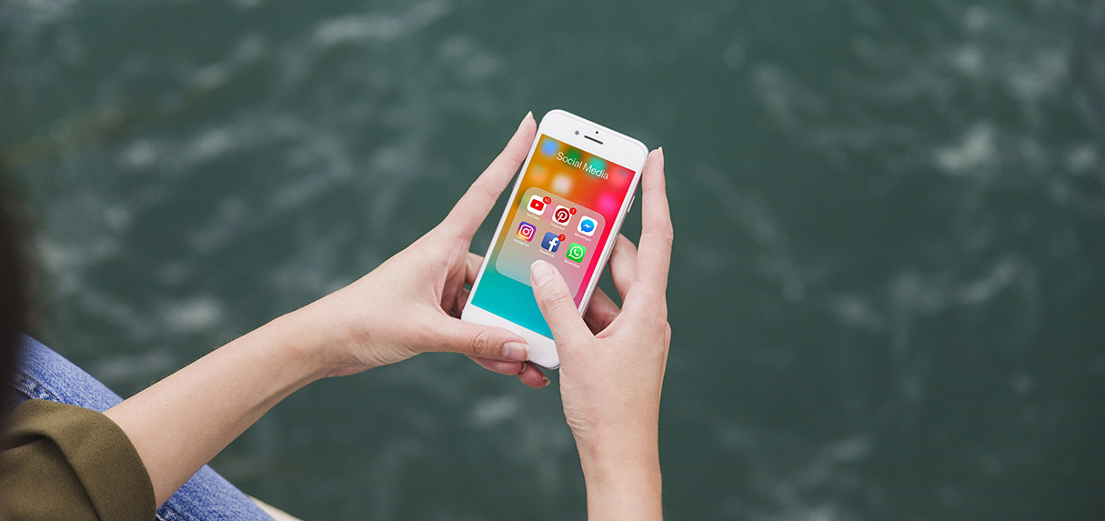 ícones de mídias sociais aparecem na tela de um smartphone que, por sua vez, é segurado por um par de mãos