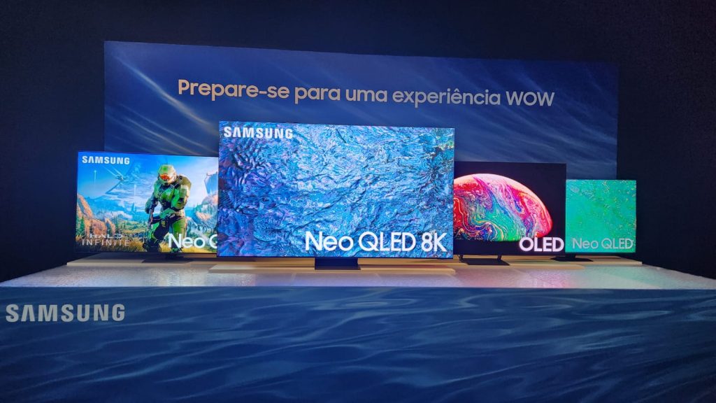 Na imagem estão quatro modelos de Smart TVs da Samsung, uma ao lado da outra, expostas em uma mesa; todas parte do portfólio de novidades da marca para 2023