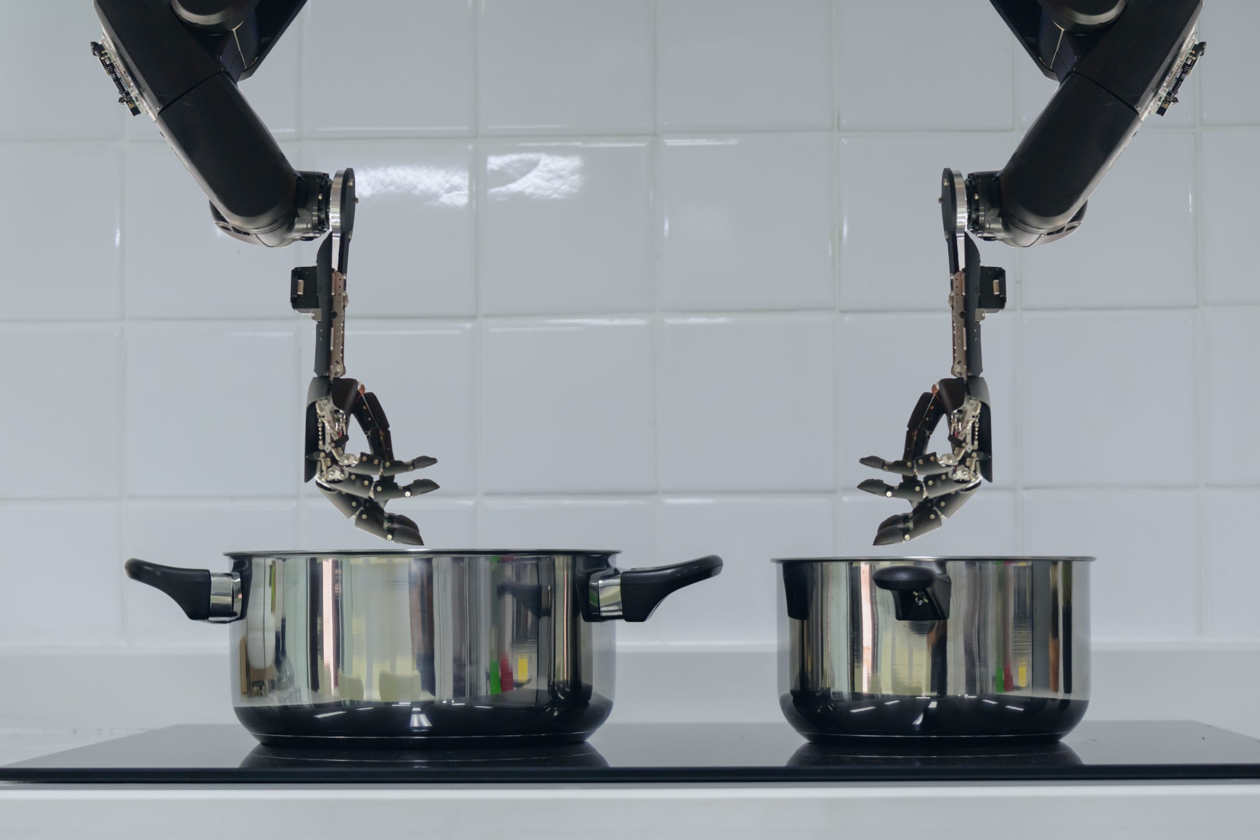 Ilustração mostra duas mãos robóticas utilizando panelas para cozinhar