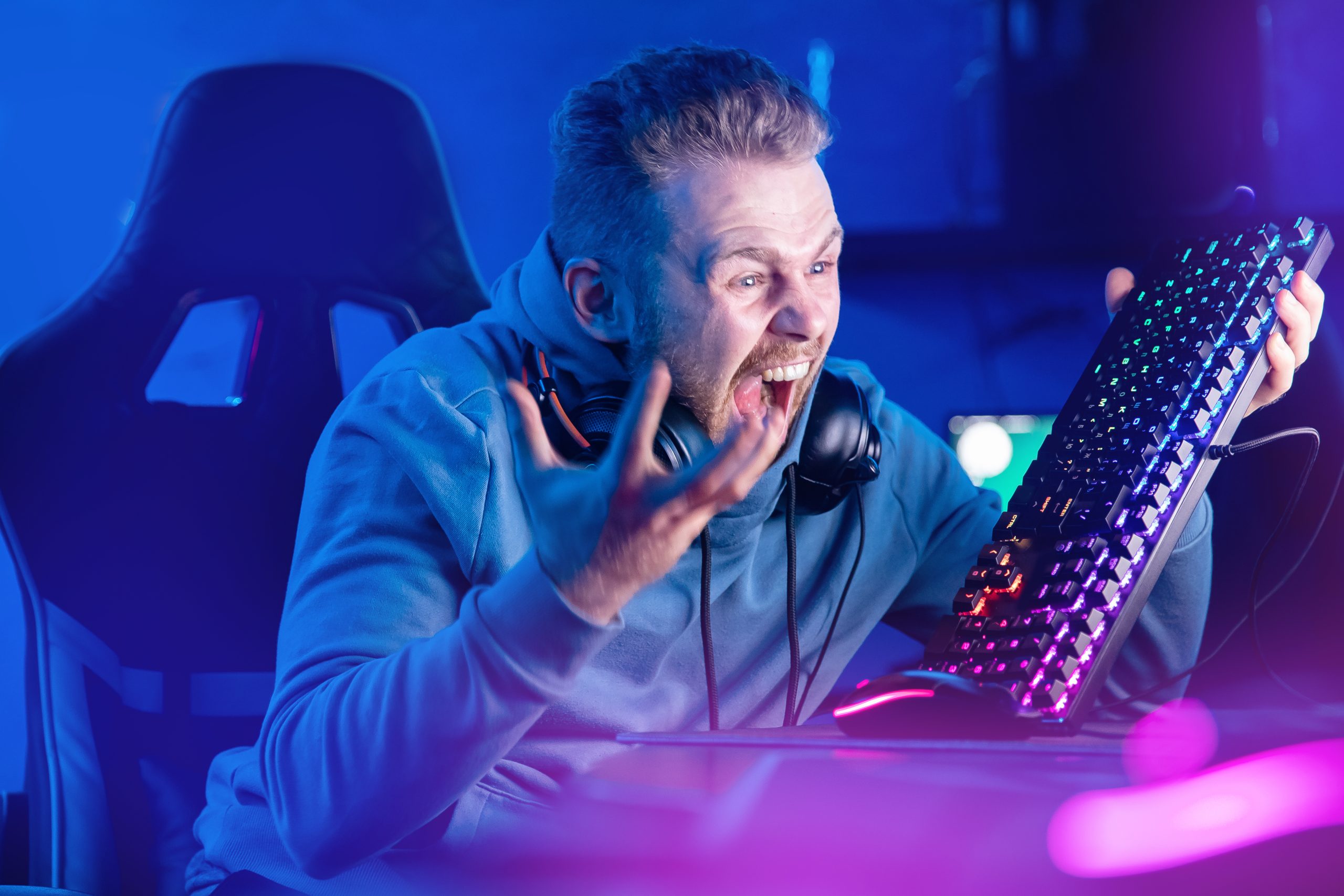 Imagem mostra um gamer zangado, segurando seu teclado e gritando com o monitor