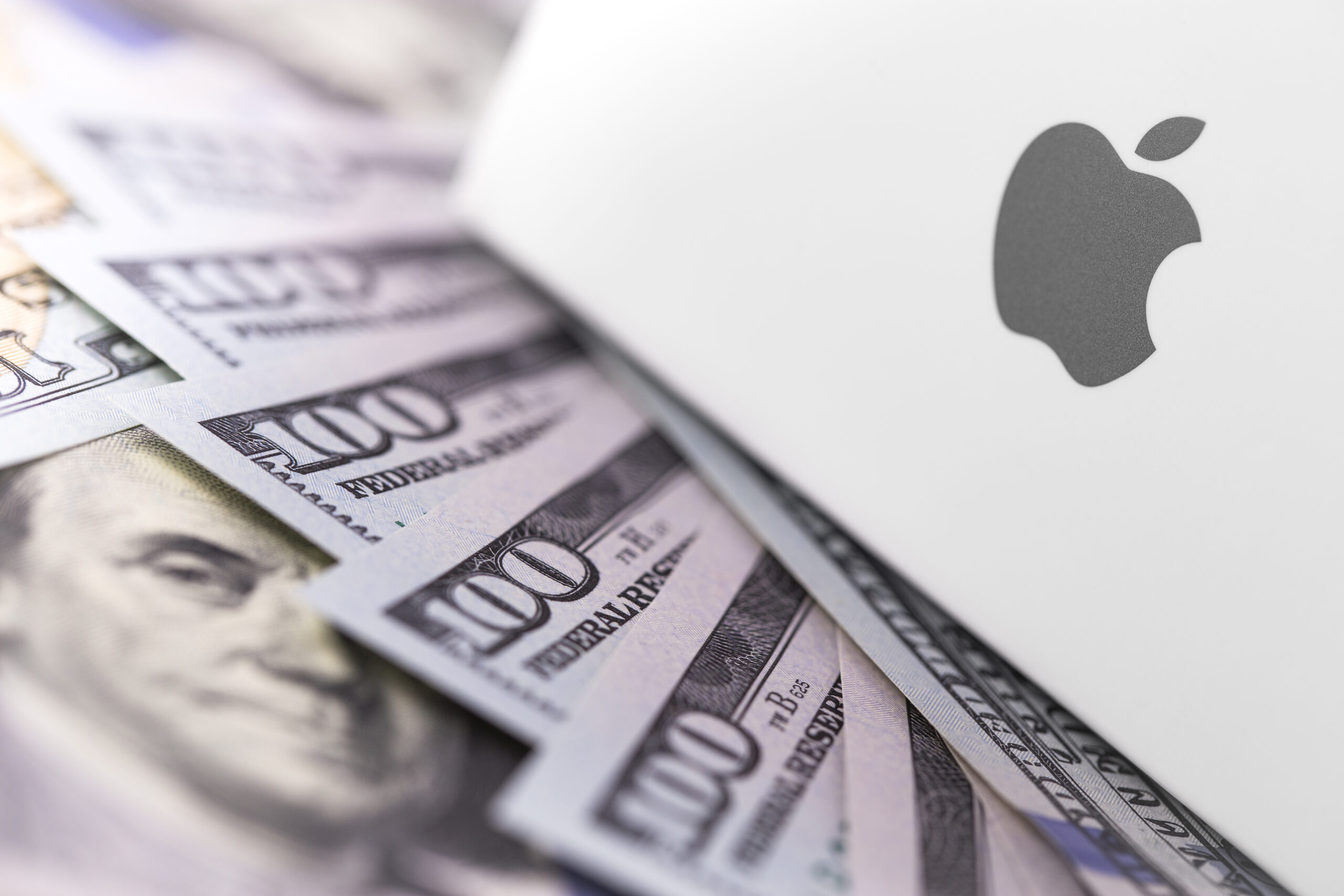 Imagem de um computador com a logomarca da Apple perto de várias notas de dólares