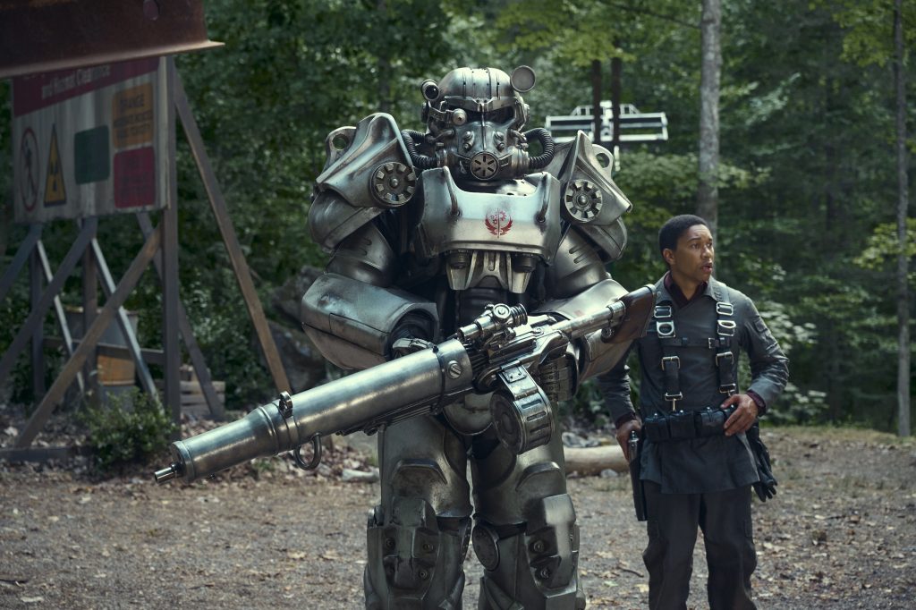 Cena da série Fallout, do Prime Video, com uma pessoa vestida no icônico exoesqueleto Power Armor do videogame, ao lado do ator Aaron Moten - que interpreta Maximus.