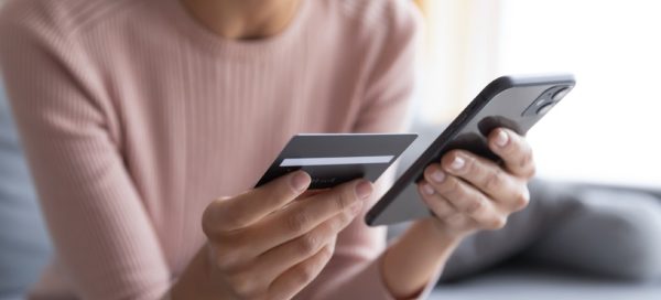 Mãos femininas segurando cartão de crédito e smartphone, ilustrando um meio de compra online, as compras via app