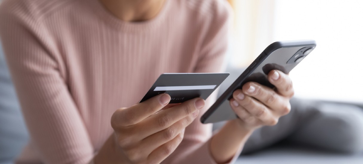 Mãos femininas segurando cartão de crédito e smartphone, ilustrando um meio de compra online, as compras via app