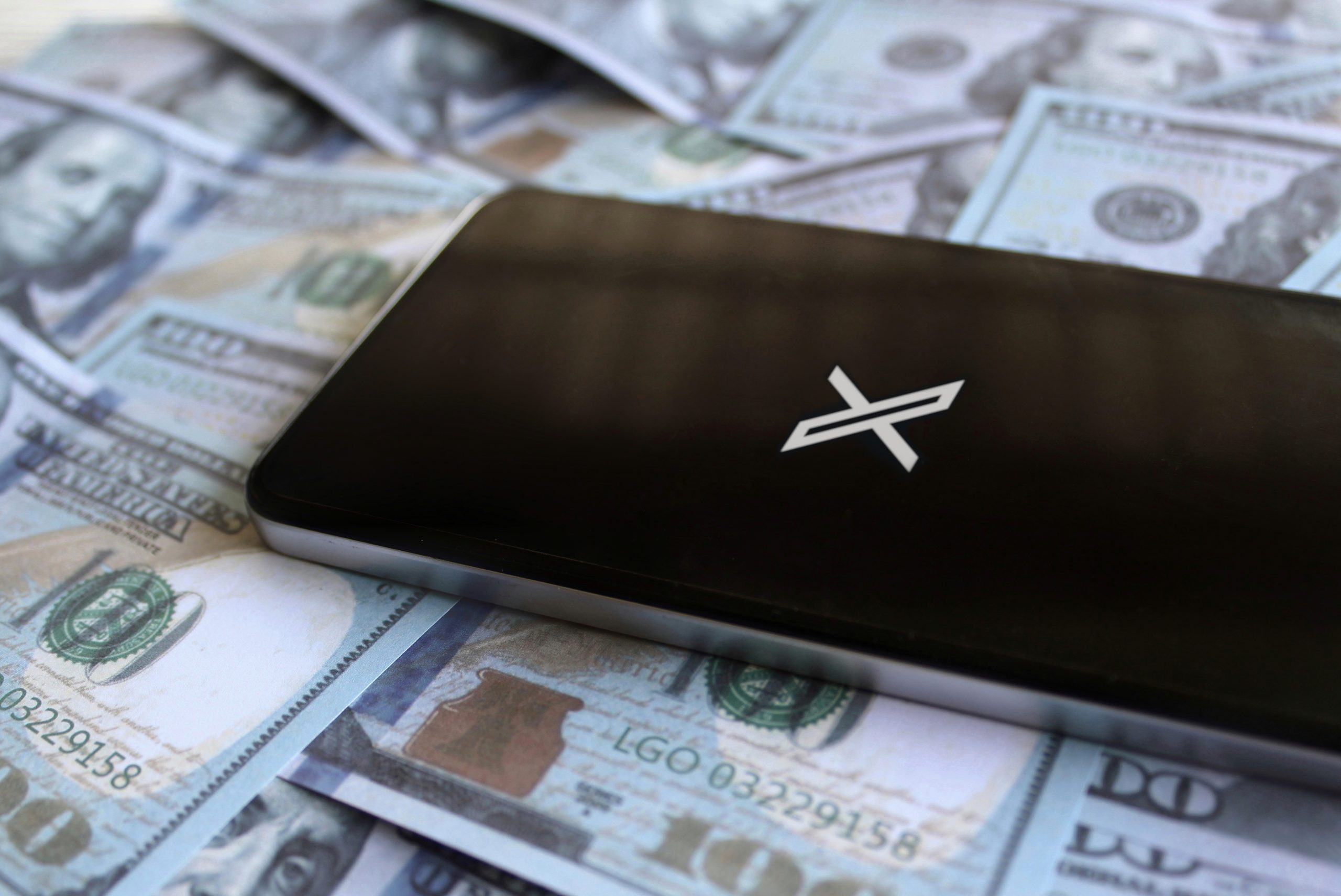Imagem mostra o X em um smartphone em meio a várias notas de dólares americanos