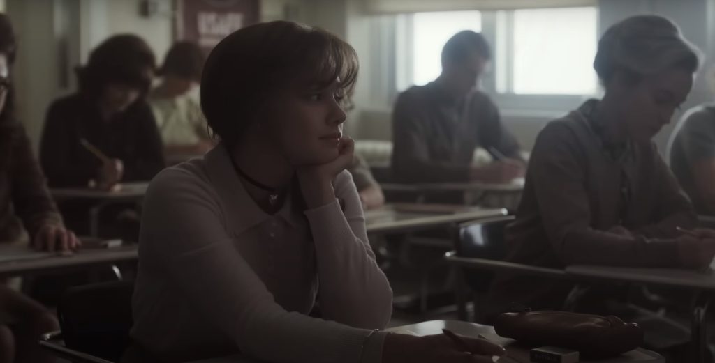 Cena de Priscilla, filme de Sofia Coppola, em que a atriz Cailee Spaeny está em uma sala de aula, olhando para o horizonte, com um cabelo longo e franja, vestindo uma blusinha de manga longa