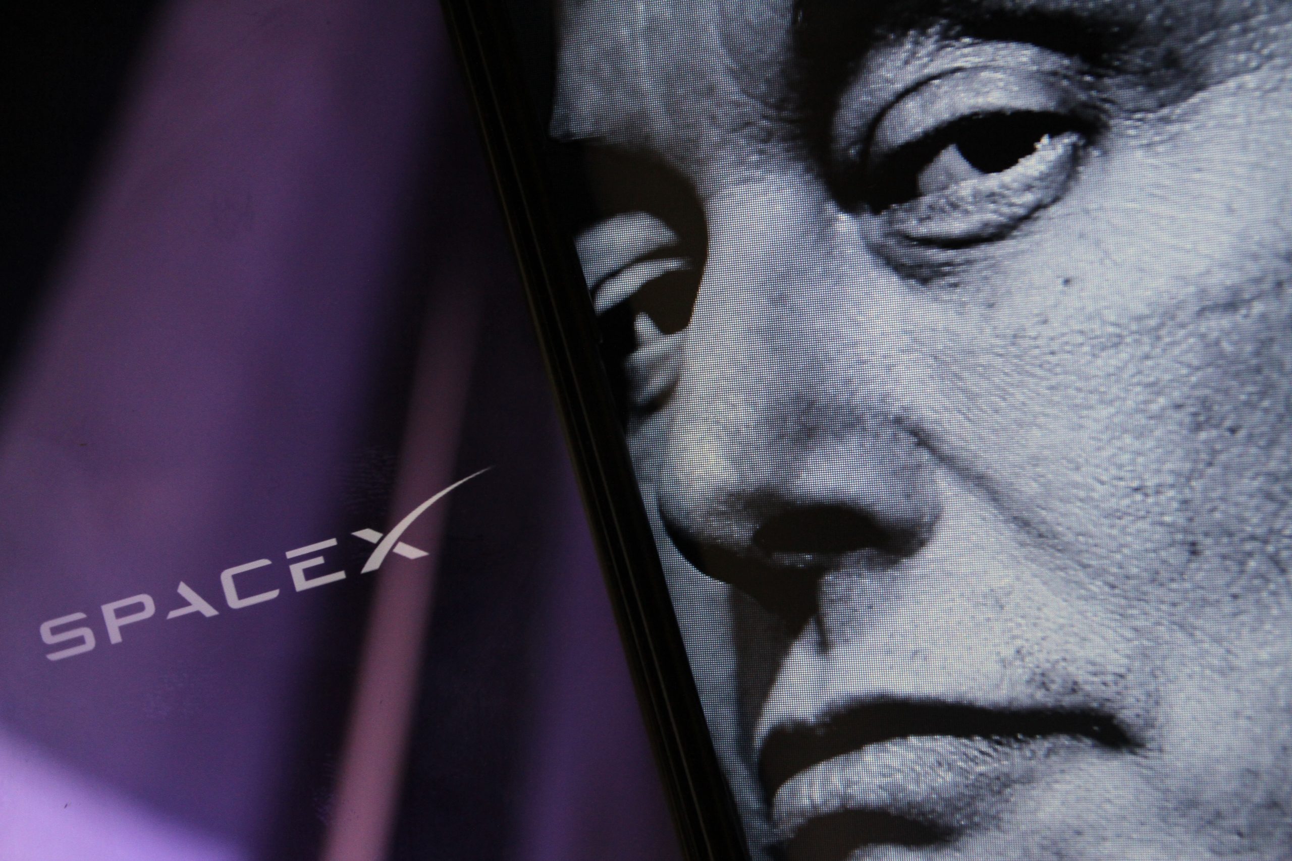 Nesta ilustração, a logomarca da SpaceX pode ser vista na tela de um smartphone ao fundo, com a imagem do rosto de Elon Musk em preto e branco exibida à frente